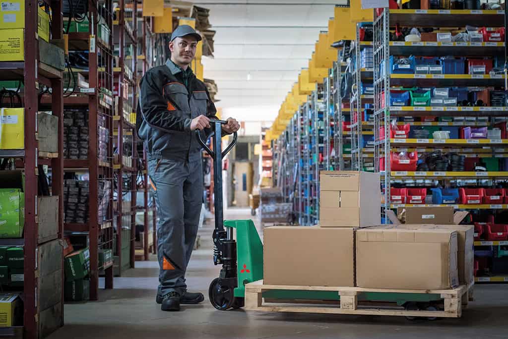 Employé utilisant une transpalette électrique dans un entrepôt de stockage.